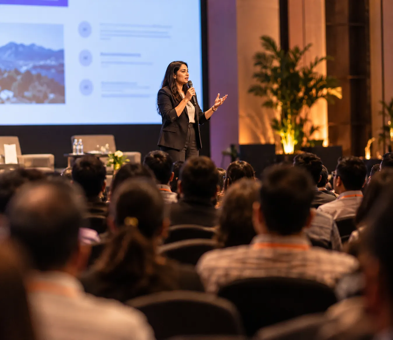 Speaker addressing a full conference audience, seen from among the seated attendees